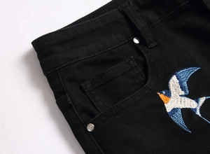 Close-up of colorful swallow embroidery on black denim pocket with silver rivets