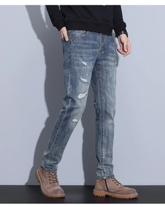 Detail view of men's slim fit blue jeans with distressed holes and paint splatter design