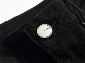 Macro shot of a silver metal button with JEANS engraving on black denim jeans