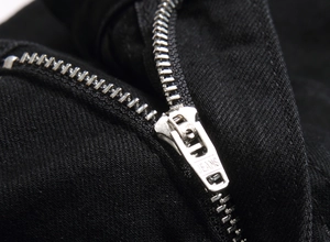Macro shot of black denim jeans showing silver metal zipper detail with JEANS engraving