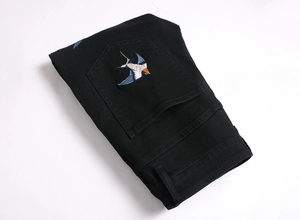 Detail of colorful swallow bird embroidery on the back pocket of black denim slim fit pants