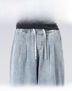 Dettaglio dei jeans in denim lavaggio chiaro con vita elasticizzata, coulisse e pieghe