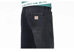 Détail d'un jean noir délavé présentant une poche arrière avec un écusson numéro sept