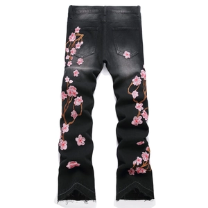 Men's washed black flare jeans with pink floral embroidery and raw hems, back view
