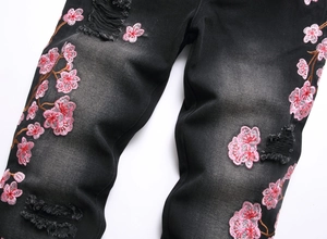 Detailed close-up of pink floral embroidery and distressed ripped denim on black jeans