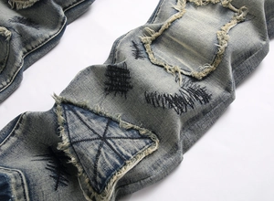 Détails du jean bleu délavé avec empiècements usés et broderies géométriques