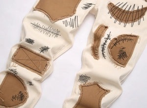 Detail of off-white street pants featuring brown distressed patches and black embroidery