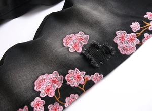 Close-up of pink cherry blossom embroidery and distressed details on black denim flare jeans