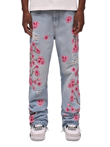 Détail du jean évasé bleu pour homme avec broderie fleur de cerisier rose et finitions usées