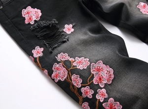 Macro detail of pink cherry blossom embroidery and distressed rips on black denim jeans