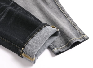 Detail of color-block denim trousers featuring yellow stitching and folded hem cuff