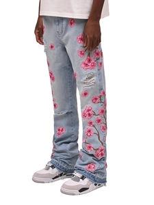 Gros plan sur la broderie de cerisier rose et les détails usés sur ce jean bleu clair