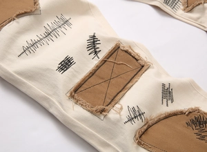 Detail of street-style beige denim with brown frayed patches and black X embroidery