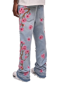 Détail de broderie cerisier rose et ourlet effiloché sur un jean flare bleu clair