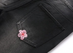 Detail of pink cherry blossom embroidery on black washed denim jeans back pocket