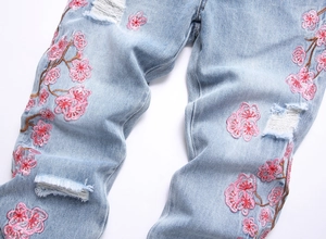 Détail d'un jean bleu clair avec broderie de fleurs de cerisier roses et ourlet effiloché