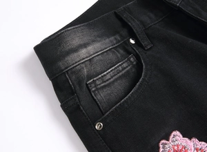 Close-up of floral embroidery on men flared jeans with metal rivets and washed denim texture