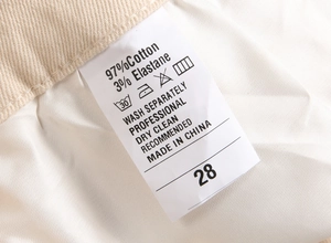 Detailed fabric care label showing 97% cotton material and size 28 on beige twill pants