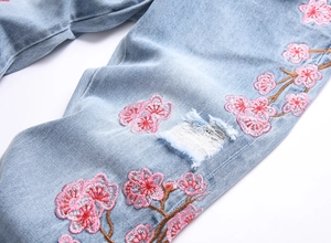 Détails de broderie cerisier rose et texture déchirée sur un jean en denim bleu clair