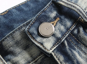Gros plan détaillé d'un bouton métallique argenté gravé JEANS sur un pantalon en jean