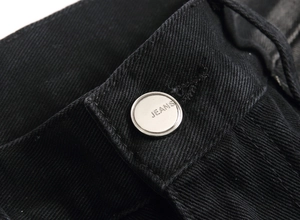 Detailed close-up of a silver jeans button on premium black twill denim fabric