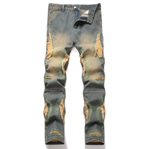 Vintage distressed blue jeans with green embroidery around large ripped knee holes