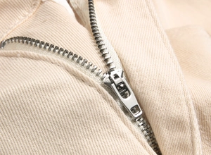 Close-up of a silver metal zipper on cream twill cotton fabric of slim flare pants