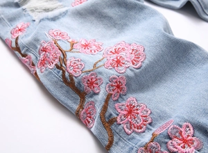 Détail de la broderie florale rose et texture denim usée sur jean évasé pour hommes
