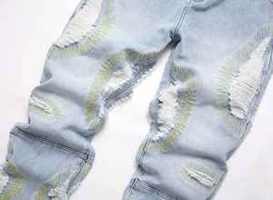 Close-up of light blue washed jeans with distressed holes and yellow embroidery details