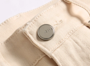 Detail of silver metal button with JEANS engraving on beige slim fit trousers