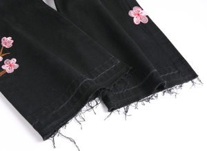 Detail of pink cherry blossom embroidery on black raw hem denim jeans for men