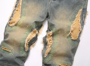 Detail of distressed jeans showing ripped denim with khaki patch and green zigzag stitching