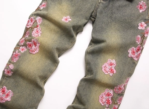Detail showing pink cherry blossom embroidery on washed vintage green flare denim jeans