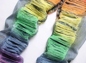 Close-up of rainbow gradient fringe and heavy distressed details on light blue denim jeans