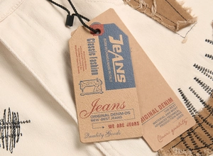 Detail of off-white denim with black embroidery, brown distressed patch and vintage paper tag