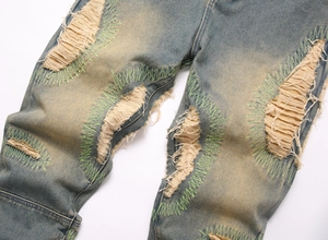 Detail of vintage washed blue jeans featuring distressed rips and neon green zigzag stitching