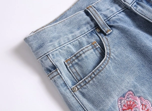 Gros plan détaillé sur la broderie de cerisier rose et rivets sur jean bleu évasé