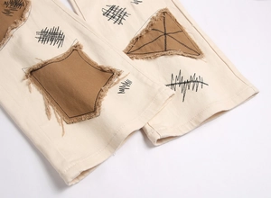 Detail of street-style beige pants featuring distressed patches and geometric embroidery
