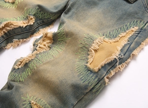 Detail of vintage washed denim jeans with distressed holes and green zigzag stitching