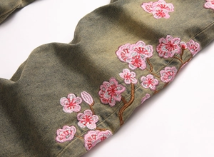 Detail of pink floral embroidery and vintage yellow-green wash on denim jeans