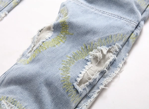 Detail of distressed light blue jeans featuring ripped holes and yellow zigzag embroidery