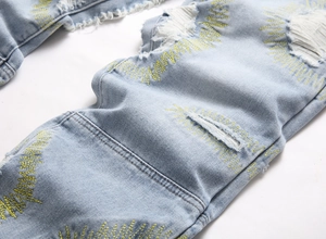 Close-up of distressed light blue jeans featuring yellow Z-stitch embroidery detail