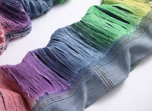 Detail of blue denim jeans featuring vibrant multi-color gradient fringe and distressed tassels