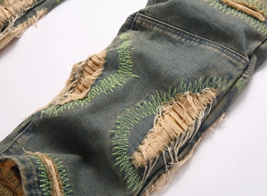 Detail of distressed blue denim with heavy ripping and fluorescent green stitching details