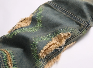 Detail of distressed blue jeans with yellow fringe rips and neon green zigzag stitching