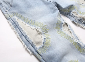 Detail shot of light blue jeans with distressed holes and yellow zigzag embroidery