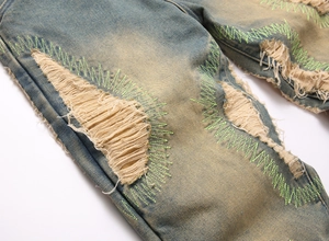 Close-up of ripped denim jeans with distressed holes and neon green embroidery detail