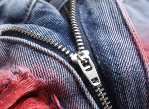 Detailed macro view of silver zipper and distinctive red frayed edges on denim jeans