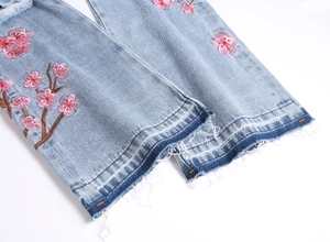 Détail de broderie florale rose et bords effilochés sur un jean en denim bleu clair