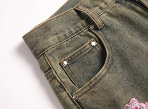 Detail of vintage washed denim jeans with pink floral embroidery and metal rivets